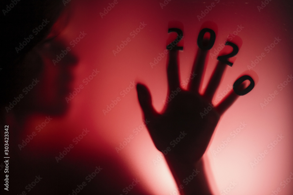 silhouette of face profile and hand with date 2020 on fingers pressed to glass of door with a red strange backlight, destruction of the stereotype happy new year