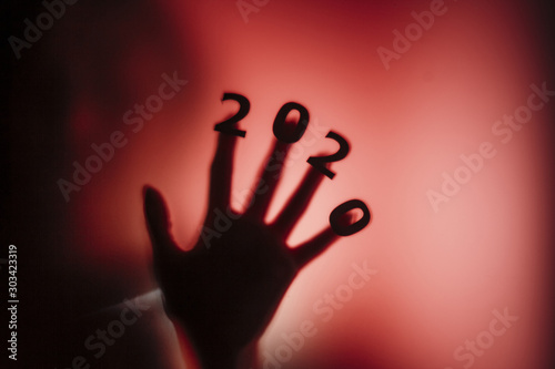 silhouette of a female hand with date on fingers pressed to glass of door with a red strange backlight, destruction of the stereotype happy new year, entering 2020 horror genre