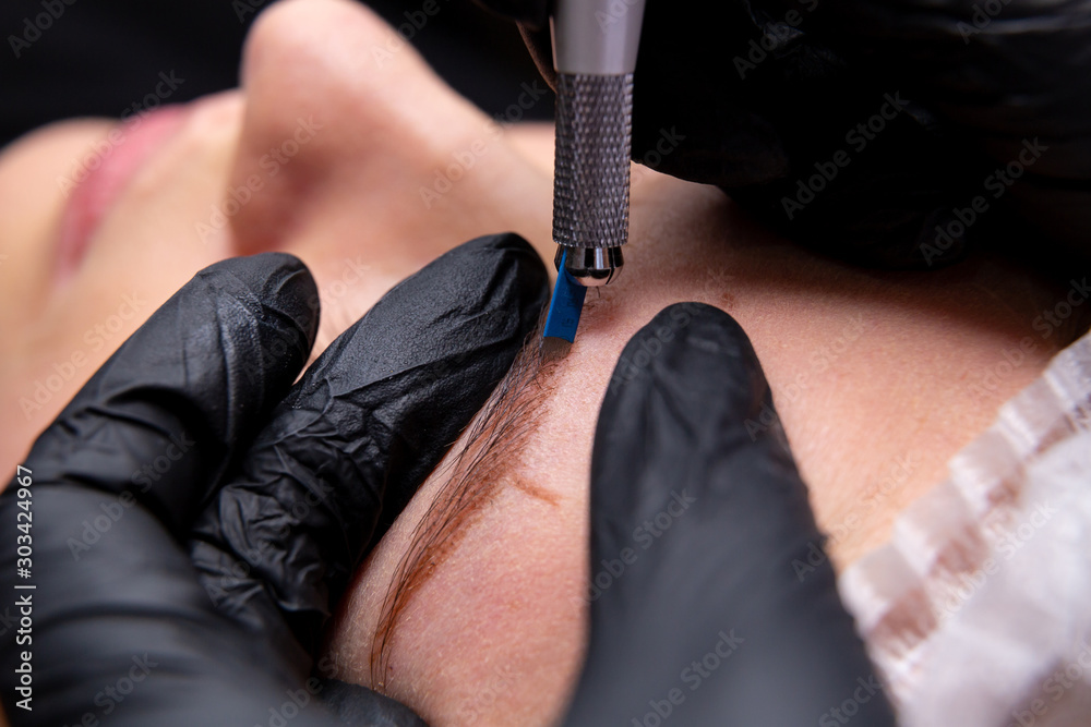 Fototapeta premium Cosmetic procedures for the treatment of eyebrows. Microblading in the beauty salon. Professional cosmetology. The process of applying the pigment.