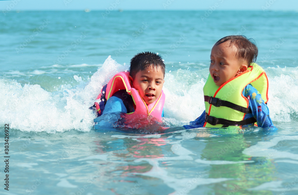 Children with life jacket playing sea waves. Kid having fun outdoors. Summer vacation time. Attractions concept.