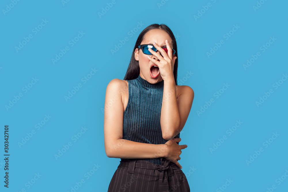 Fototapeta premium Freestyle. Young woman wearing 3d glasses standing isolated on blue covering face screaming scared horror