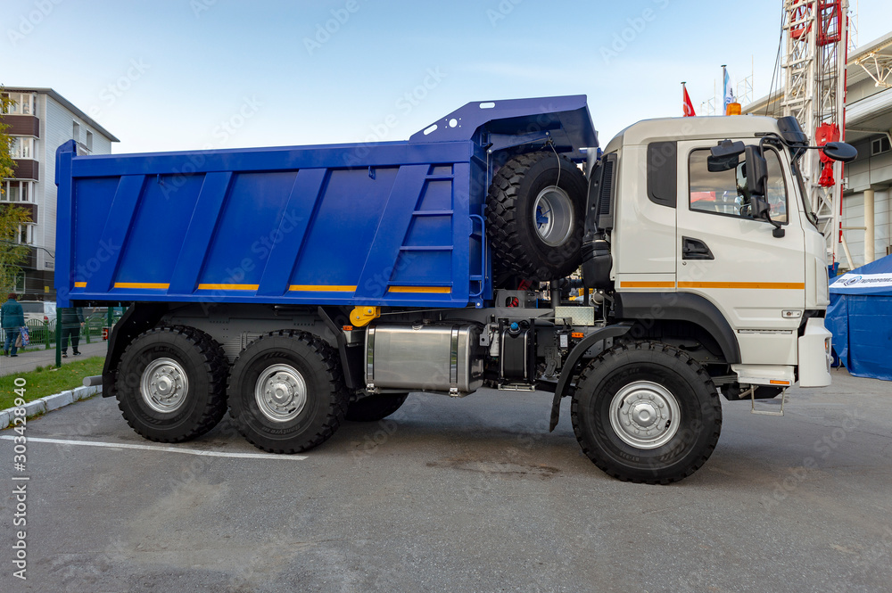 Dump truck parked in the city. White cab, blue body. Side view.