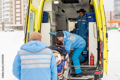 Paramedics getting stretcher with fixed unconscious man into ambulance car photo