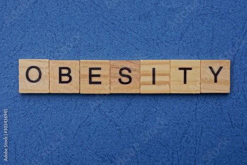 word obesity made from brown wooden letters lies on a blue table photo