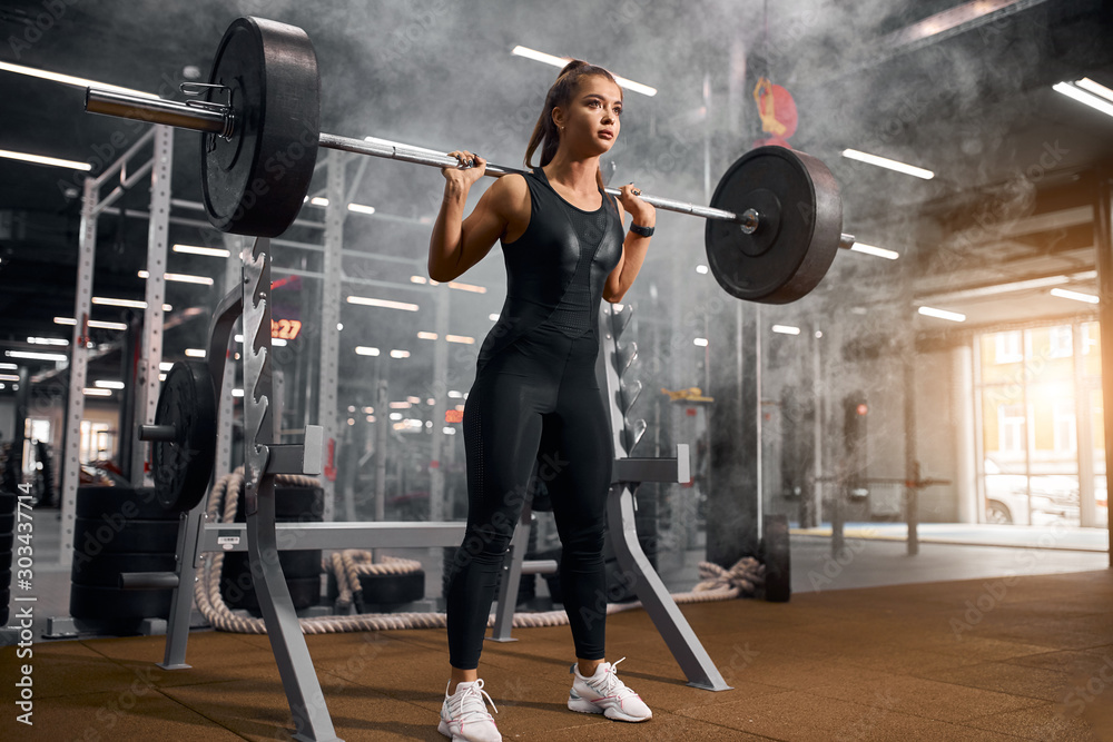 Strong female weightlifter standing in middle of big gym hall