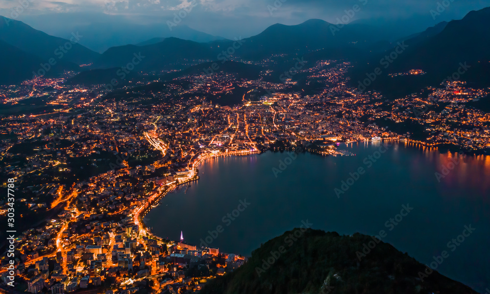 High angle aerial drone night shot of city street lights by lake in Lugano, Switzerland