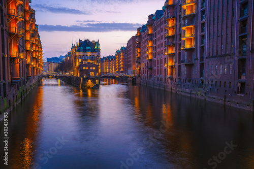 Hamburg city old port during blue hour, Germany, Europe. Historical famous warehouse district artificial illuminated. Water castle palace mirrored on river surface