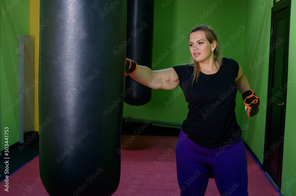 A fat woman is training kickboxing in the gym. A girl in boxing gloves beats a punching bag. Female obesity. Hard workouts for weight loss.