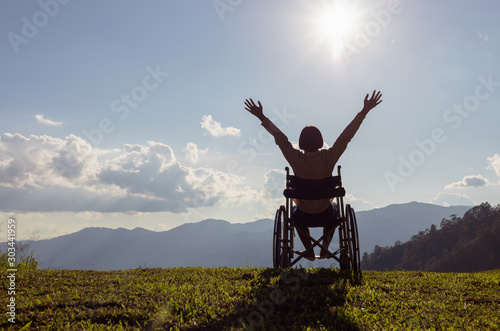 Fotografering Happy disabled child in a wheelchair and stretching hands at sunset
