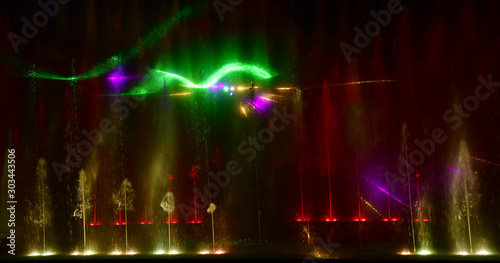 Colorful water fountains. Beautiful laser and fountain show. Large multi colored decorative dancing water jet led light fountain show at night. Dark background.