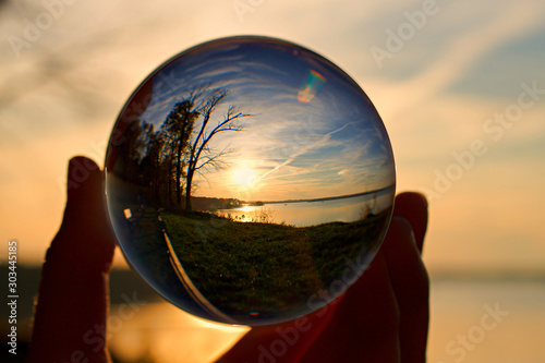 Reflection of sunset over water in a crystal ball, held by a hand © JMP Traveler