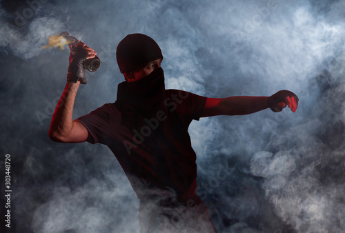 A protesting man in puffs of smoke throws a burning bottle. Studio photography photo