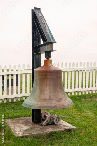 A large bell found on the grounds of the Pemaquid Point Lighthouse, located in Bristol, Lincoln County, Maine, with a white picket fence in the background. photo