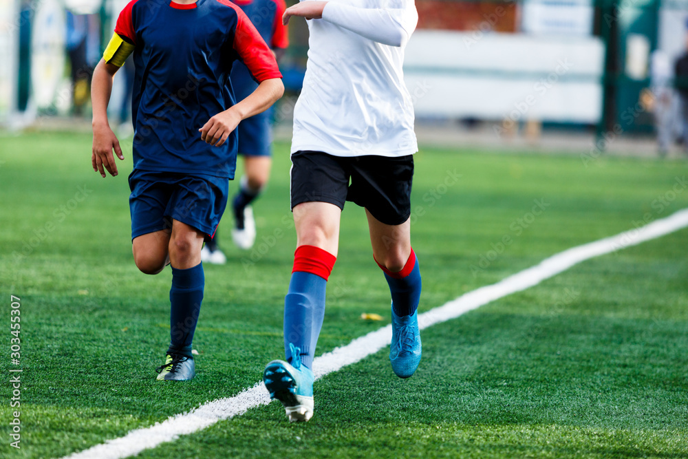 Boys in white and blue sportswear plays  football on field, dribbles ball. Young soccer players with ball on green grass. Training, football, active lifestyle for kids concept 