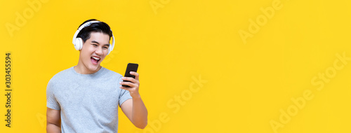 Smiling Asian man wearing headphones listening to music from smartphone