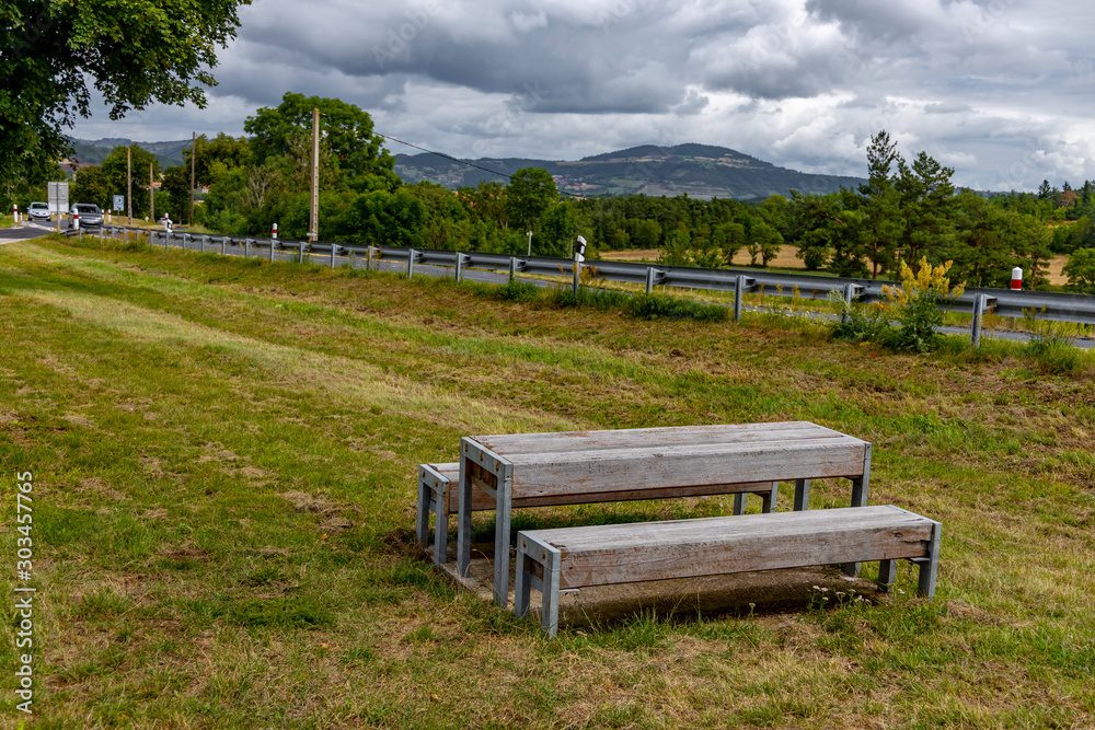 Obraz premium Benches and a table in a recreation area near the highway against a background of green grass and mountains.