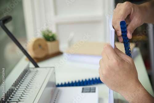 Man making report using comb binding machine - people working with stationary tools concept