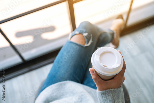 Top view image of a woman sitting and holding a paper cup of hot coffee in the morning