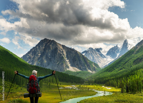 A girl with her hands up standing by the mountain river, looking at the beautiful summer landscape. Hiking, the concept of research, travel and expeditions.