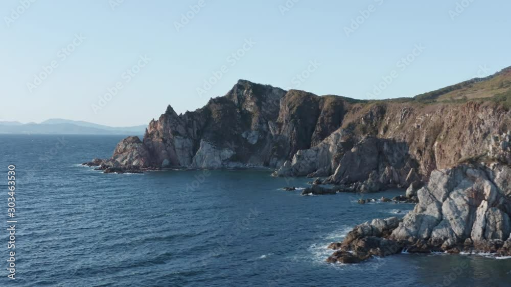 Bird's eye view of coastline with steep cliffs, underwater rocks on the sunset. Slow aerial pivot shot. Russia, Far East. Bird's eye view of coastline with steep cliffs, underwater rocks on the sunset. Slow aerial pivot shot. Russia, Far East.