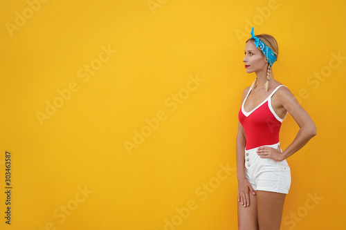 Summer urban fashion. Fun and colorful. Young pretty happy woman in shorts posing against yellow wall.