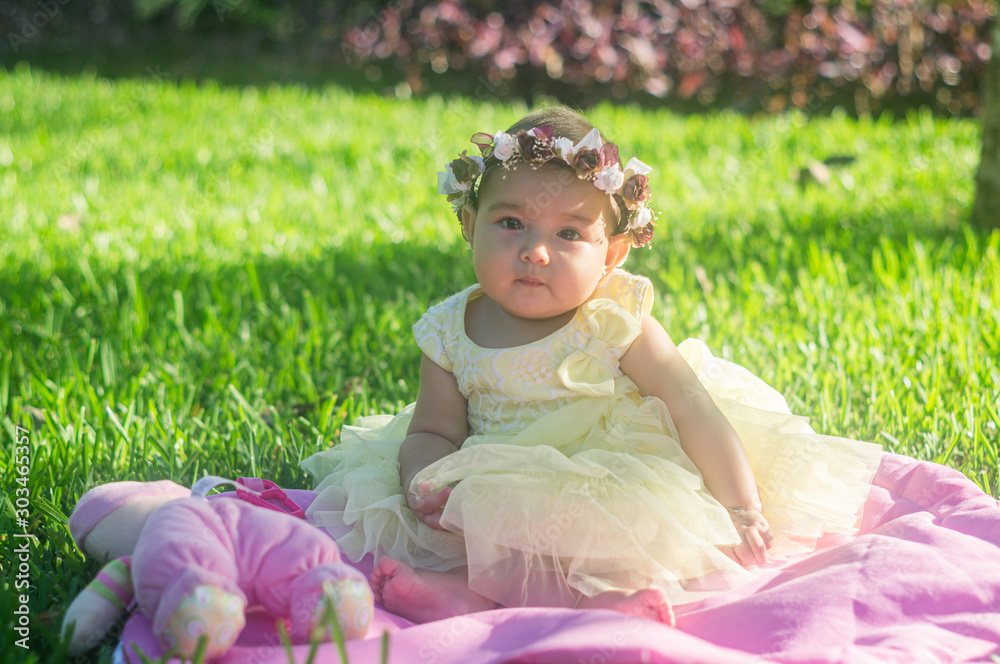 Baby wreath flowers yellow dress in the garden, sitting on pink mat on the grass look at camera Baby wreath flowers yellow dress in the garden, sitting on pink mat on the grass look at camera