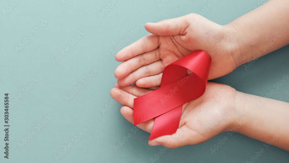 Hands holding red ribbon on red background, hiv awareness concept, world AIDS day, world hypertension day