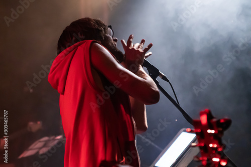 Fotografía Low angle view of a male musician is viewed from behind as he sings, Holds a mic