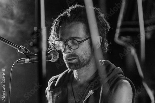 Selective focus close up on caucasian man wearing glasses as he sings deeply in the front of the microphone, black and white