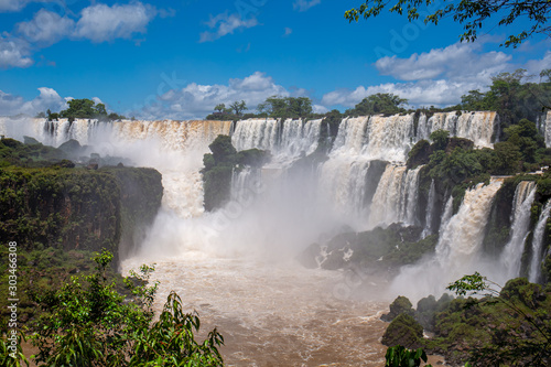 Panoramic view to cascading water falls  brown river and blue sky  Iguazu Falls  Argentina