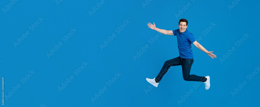 Energetic young man jumping and smiling with outstretched hands Energetic young man jumping and smiling with outstretched hands