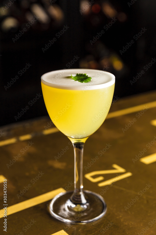 Ταπετσαρία A yellow cocktail in a nick and nora glass garnished with cilantro at the bar