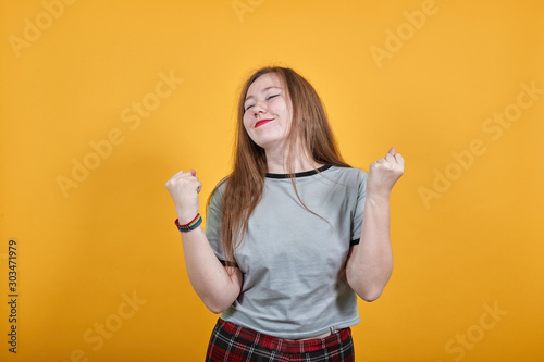Young woman standing over isolated orange background very happy and excited keeping thumbs up with arms raised, smiling for success, closed eyes.