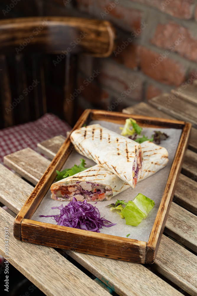 Grilled roll shawarma with chicken breast, tomatoes and red cabbage served on wooden tray
