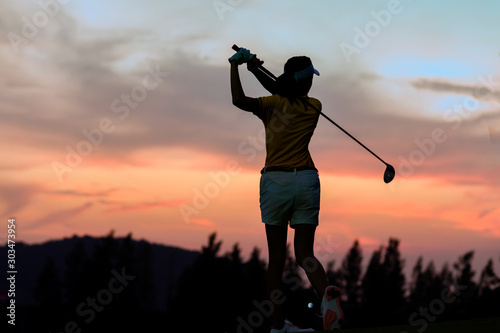 silhouette of woman golfer in an action of completed down swing hit a golf ball away to fairway in the golf course at sunset