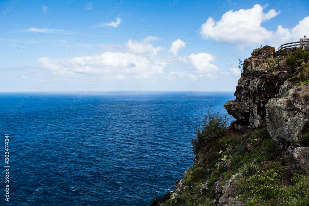 Cliff with blue ocean water and white clouds 