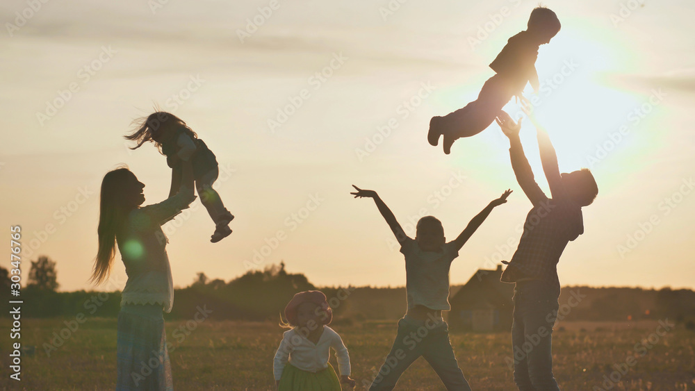 The concept of a happy large family. Happy parents tossing their children up on a sunset background. - obrazy, fototapety, plakaty 