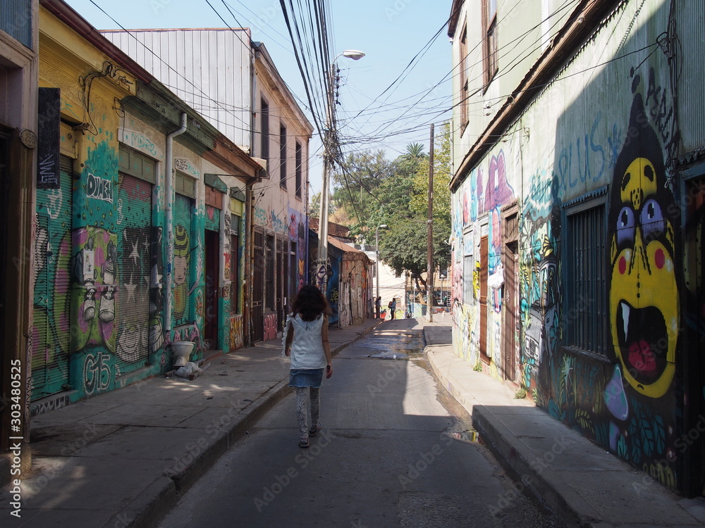 Fototapeta premium A woman walking through the city with beautifully designed walls and streets, Colorful houses and streets of the port city, Valparaiso, Chile