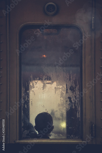Vintage train window with a silhouette of a child seen behind a wet window