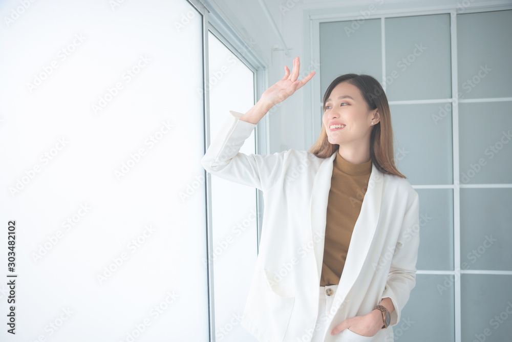 Beautiful asian woman standing in office and raising hand to covering her face from sunlight.