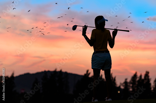 silhouette of woman golfer in an action of relxa and enjoy after hit a golf ball away to fairway in the golf course at sunset