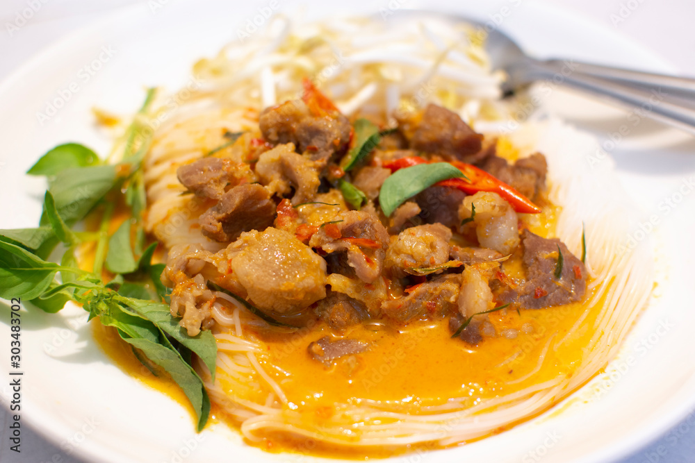 Rice noodles topped with Panang pork curry and Thai basil,Finger chilli,Bean sprouts on a white plate.