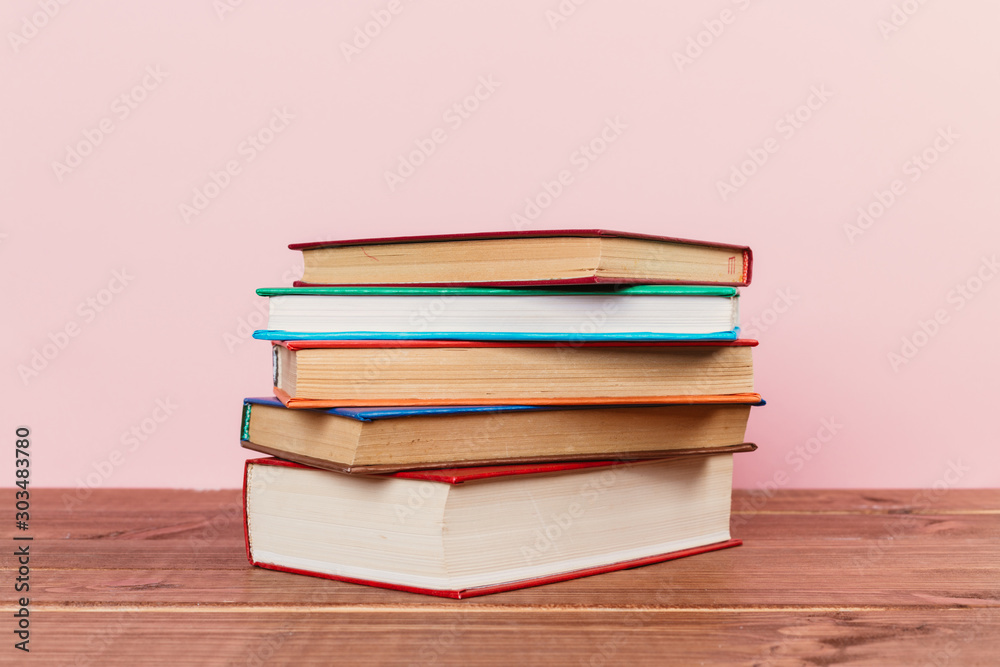 A simple composition of many hardback books, raw books on a wooden table and a pale pink background A simple composition of many hardback books, raw books on a wooden table and a pale pink background