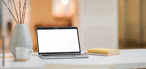 Cropped shot of comfortable workplace with mock up laptop computer, coffee cup and office supplies