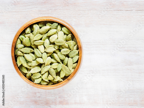 Spice Green Cardamom (Elettaria cardamomum) in a wooden cup on a white wooden background with copy space