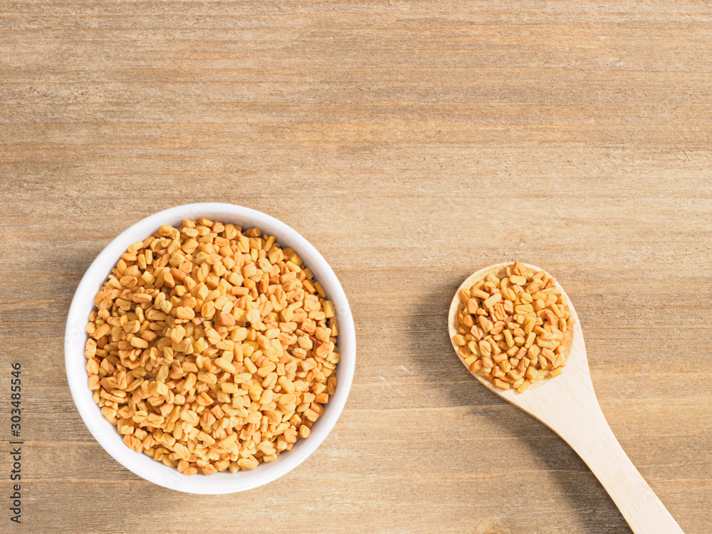Fenugreek in white bowl and spoon on a brown wooden background. Indian cuisine, ayurveda, naturopathy, modern apothecary concept Fenugreek in white bowl and spoon on a brown wooden background. Indian cuisine, ayurveda, naturopathy, modern apothecary concept