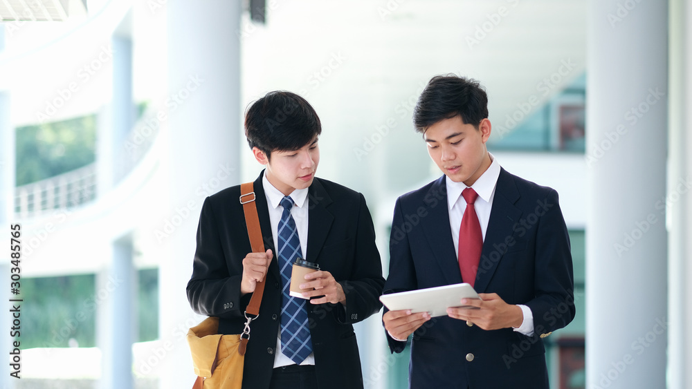  Two confident business partners walking down in office building and talking while taking coffee.