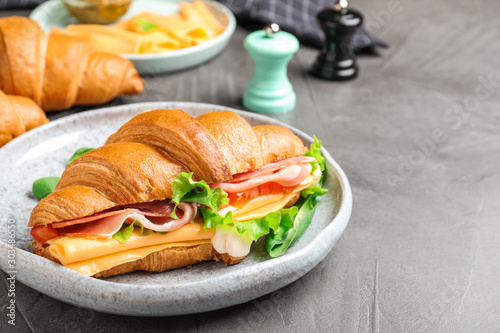 Tasty croissant sandwich with ham and cheese on grey table
