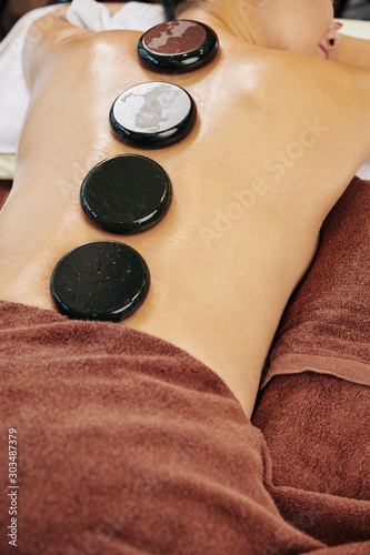 Round hot stones on back of young pretty woman relaxing in spa salon
