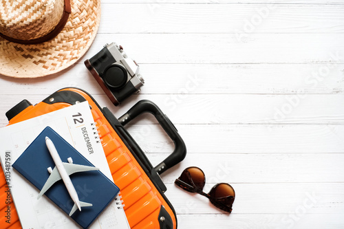 Flat lay holiday planing and traveler concept on white wooden background with passport and plane is on calendar and orange suitcase, accessory, Top view with copy space